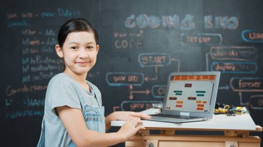 Asyalı öğrenci mühendislik kodları ya da masadaki ekipmanlarla birlikte kameraya doğru dönün. Güvertede dizüstü bilgisayar kullanarak çalışan tatlı bir kız. Yaratıcı eğitim konsepti. Öğretim.