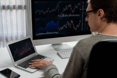 Stresli iş adamı günü modern ofisteki dinamik borsa grafiğine bakıyor, veri tabanı bilgisayarını ve bilgisayarını evden çalışırken karşılaştırıyor. Bireysel.