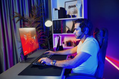 Kulaklık takan akıllı oyun flaması hafta sonu neon dijital siber ışıklandırma odasında son yaşam tarzı yarışmasında şampiyon olmak için bilgisayar ekranında araba yarışı oynamaktan zevk alır. Tahmin et..