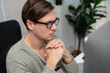 Modern ofiste oturan akıllı bir ofis çalışanı, ciddi bir yüz ifadesi olan, güzel görünümlü gözlük takan bir kamera. Yeni bir profil üzerinde sıradan bir günde çalışan iş adamı kavramı. Bireysel.