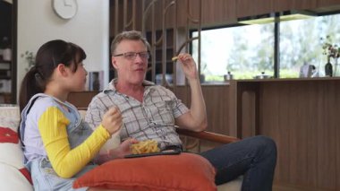 Grandfather and granddaughter eat french fries watch interesting entertainment on TV. Senior use technology communicate with young generation cross generation gap strengthen family bond. Divergence.