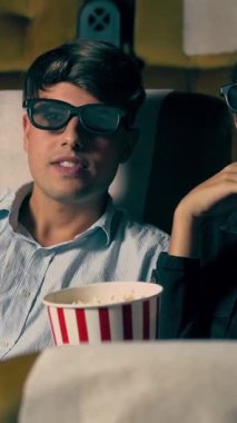 Sinemada üç boyutlu gözlüklü bir kadın ve erkek film izliyor. Ekrana bakar, heyecan verici ve patlamış mısır yer.