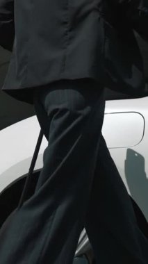 İlerici iş kadını şehir merkezinde dolaşmadan önce şarj cihazından elektrikli arabasına şarj prizi takıyor. Çevre dostu şarj edilebilir araba, sürdürülebilir ve temiz enerjiyle çalışıyor..