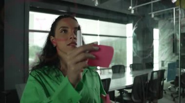 Fikirlerini paylaşmak için cam duvara yapışkan notlar yapıştıran zeki, yetenekli İspanyol menajer. Ofisteki cam tahtada yapışkan notlar kullanarak iş planı yapan profesyonel bir iş kadını. Yönlendirici.