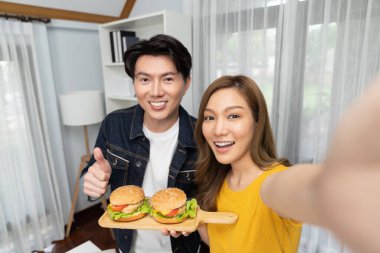 Gülümseyen sunucu şefler akıllı telefonlarıyla fotoğraf çekiyorlar. Özçekim yoluyla. Yemek programında çift hamburger tutuyorlar. İnfobahn.