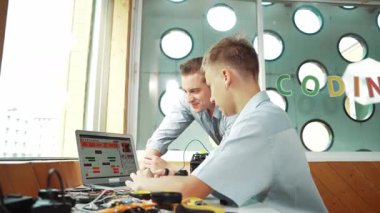Akıllı öğrenci kodlama programı ve araba modelinden yetenekli öğretmene. Genç, elektronik ekipmanların etrafa saçıldığı masadaki robot makineler için bilgisayar kullanıyor. Öğretim
