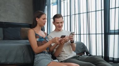 Genç çift, kredi kartıyla ödemek için internet üzerinden ödeme uygulaması ve dijital cüzdan kullanarak yatak odasında oturuyor. Mobil internet üzerinden alışveriş ve modern alımlar. Düzenle