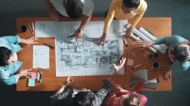 Zeki inşaat mühendisi ekibinin toplantı masasında plan, renk paleti ve ekipmanlarla fikir alışverişinde bulunurken el sıkışması. Çeşitli insanların üst hava görüntüsü el sıkışıyor. Birlik. Sempozyum.
