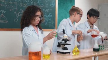 Çocuklar laboratuvarda karatahta başında dururken fen dersinde deney yapıyorlar. Mutlu öğrenci biyokimyasal sıvıyı keşfederken ve incelerken ve karıştırırken. Pedagoji.