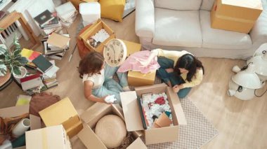 Taşındığı gün karton kutudan mobilyaları çıkartırken oturma odasında oturan çift. Mutlu aşığın yeni daireye taşınırken birlikte yardım ve destek verdiğinin en üst görüntüsü. Yeniden yerleştirme. Myrmidon.