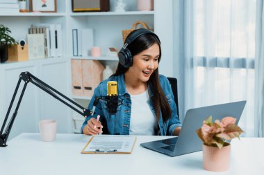 Sosyal medyada kulaklıkla canlı yayın yapan Asyalı sunucu modern stüdyoda yaşam koçluğu veya pazarlama dinleyicilerini selamlıyor. Taktik.