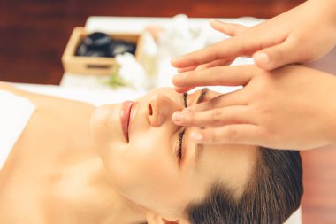 Yakın plan kadın stres önleyici kafa masajı yapmaktan ve lüks tatil beldesi veya otel spa salonundaki modern ışık ortamında yüz güzelliği eğlencelerini şımartmaktan zevk alıyor. Sessiz.