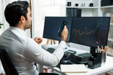 Akıllı telefondan akıllı telefon arayan tüccar işadamı, bilgisayardaki dinamik borsa yatırım ekranını analiz ediyor ve modern merkez ofisteki en kârlı finansal teknoloji pazarına yatırım yapıyor. Tahmin et..