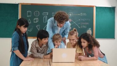 Kafkas öğretmeni ve çeşitli öğrenciler sınıfta dizüstü bilgisayara bakıyor. Kodlama programını öğrenen ya da öğretmenlik yaparken yazılım kullanarak oluşturulan çok kültürlü çocuklar. Pedagoji.