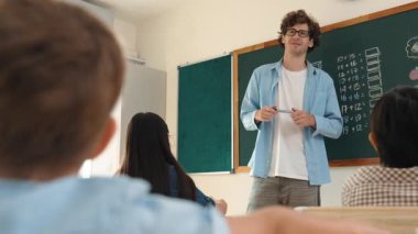 Matematik formülü veya teorisi ile karatahtanın önünde dururken sınıfın etrafına bakan profesyonel akıl hocası. Çeşitli ilköğretim öğrencileri matematik dersinde öğreniyor, çalışıyor ve oturuyor. Pedagoji.