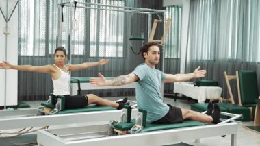 Pilates reformatör makinelerinde senkronize kol uzantıları yapan iki müşteri. Mutlu pilates partnerleri, esnekliği arttırmak ve dengeyi ve kontrolü sağlamak için reformcunun üzerine oturdular. Alışkanlık.