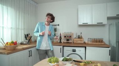 Mutlu baba yemek pişirirken müziğe geçiyor ve modern mutfakta öğle yemeği hazırlıyor. Aktif baba, sebze ve mutfak gereçleri ile çevrili sağlıklı yemek ya da salata yaparken şarkıyla dans ediyor. Pedagoji.