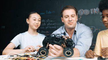 Akıllı öğretmen araba modelini farklı öğrencilere denetliyor. Karışık ırk dinleyicisi olan liseli çocuklar masadaki dizüstü bilgisayarlı ve kablolu robot model sistemini açıklıyor. Öğretim.