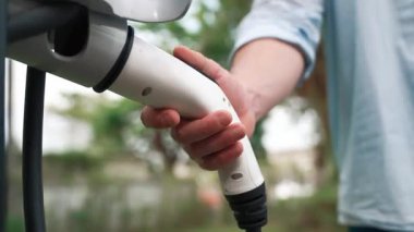 Modern çevre dostu adam EV şarj istasyonundan elektrikli aracı şarj ediyor. EV araba teknolojisi ev sakinleri için gelecekte çevresel sürdürülebilirlik için kullanılıyor. Titiz