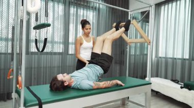 Cadillac ekipmanları üzerinde bacak kaldırma egzersizinde müşteriye yardımcı olan yetenekli pilates eğitmeni. Kadın antrenör, Cadillac 'ın bacak gerdirme hareketine yardım ediyor. Temel bağlantıyı geliştirmek için, bacak esnekliği için. Alışkanlık.