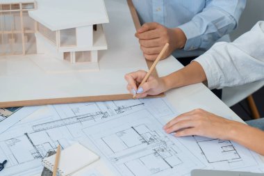 Asyalı kooperatif iş arkadaşı ev modelini ev modeliyle ve bina planıyla birlikte masaya koyarken, profesyonel güzel mimarın el yapımı taslaklarının en üst görüntüsü. Tertemiz..