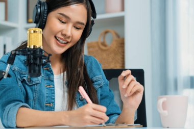 Sosyal medyada kulaklıkla canlı yayın yapan Asyalı sunucu modern stüdyoda yaşam koçluğu veya pazarlama dinleyicilerini selamlıyor. Taktik.