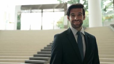 Akıllı iş adamı merdivenlerde kameraya bakıyor. İş elbisesi giyerken kameraya gülümseyen başarılı adamın yakın çekimi. Yönetici, kameraya bak. Hareket eden kamera. Sevinçli..