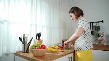 Enerjik anne, mutfak malzemeleri ile çevrili sebzeleri doğrarken modern mutfakta kahvaltı için salata yapıyor. Akıllı kadın temizlikçi yemek pişirir ve yemek hazırlar. Sağlıklı bir yaşam tarzı. Pedagoji.