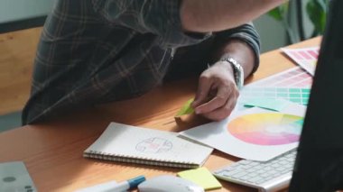 Toplantıda profesyonel tasarımcı yazma ve logo grafiği tasarlama. Renkli paletler üzerinde çalışan iş adamlarının yakınlaşması ve masaya kağıt ve ekipman ile yapışkan notlar yazmak. Sempozyum.
