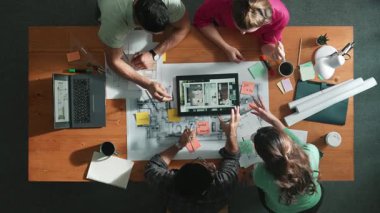 İnşaat mühendislerinin masa başında proje planıyla otururken tablet kullanarak ev yapısını dizayn etmelerine tepeden aşağı bir bakış açısı. Ekip planlama ve inşaat hakkındaki fikirlerin havadan görüşü. Sempozyum.