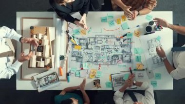 Yöneticinin el sıkıştığı ve planlar ve ev modeliyle toplantı masasında sözleşme yaptığı en üst hava görüntüsü. Çeşitli insanlar birlikte çalışıyor ve başarılı bir projeyi kutluyorlar. Hizalama.