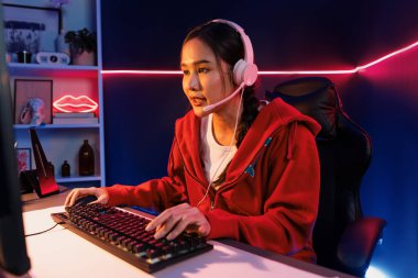 Güzel Asyalı kız flama kanalının sunucu kanalı çevrimiçi oyun odaklı kulaklık takıyor pastel renkli kulaklıklar takarak izleyicilerle çevrimiçi konuşuyor. Esport yetenekli takım oyuncuları neon mavi odada. Taktik.