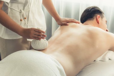 Sıcak bitkisel top spa masaj vücut tedavisi, masör erkek vücuduna nazikçe şifalı bitki torbası bastırıyor. Aromaterapi dinlenme sükuneti ve sükuneti kaplıca salonundaki atmosferi aydınlatıyor. Sessiz.