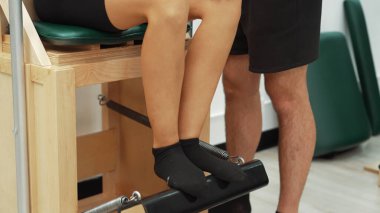 Wunda Sandalyesi ekipmanına pilates dersi veren rehber öğretmen. Antrenör pilates wunda sandalyesini kullanırken bacağa bastırarak çekirdek dengesini ve alt vücudu geliştirmek için poz veriyor. Alışkanlık.
