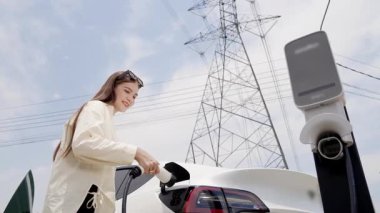 Alttaki görüntüde kadın EV araba aküsünü şarj ediyor elektrik şebekesine bağlanıyor elektrik endüstrisi çevre dostu araç için elektrik endüstrisi olarak. Yararlı