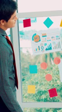 İş adamları ofisteki proje planlama kurulunda çalışıyor ve proje gelişimini analiz etmek için iş arkadaşlarıyla sohbet ediyorlar. Düzenli olması için cam duvara yapıştırılmış yapışkan notlar kullanıyorlar. .