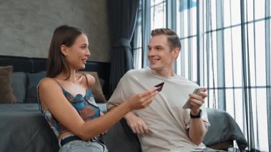 Genç çift, kredi kartıyla ödemek için internet üzerinden ödeme uygulaması ve dijital cüzdan kullanarak yatak odasında oturuyor. Mobil internet üzerinden alışveriş ve modern alımlar. Düzenle