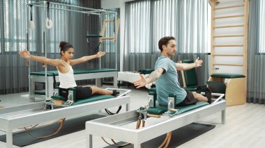 Pilates reformatör makinelerinde senkronize kol uzantıları yapan iki müşteri. Mutlu pilates partnerleri, esnekliği arttırmak ve dengeyi ve kontrolü sağlamak için reformcunun üzerine oturdular. Alışkanlık.