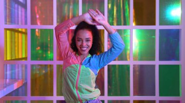 Neşeli İspanyol kız gece kulübünde renkli giysiler giyerken neon ışıkta müzik eşliğinde hareket ediyor. Sokak dansçısı kameraya bakarken hareketli adımlar atıyor. Mutluluk.
