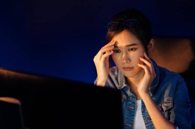 Stresli, genç, güzel Asyalı yaratıcı proje yaratıcısı sosyal medyayı araştırmak için bilgisayara bakıyor ve geceleri daha çok neon modern ofisin planlama kanalı stratejisine ulaşılıyor. Taktik.