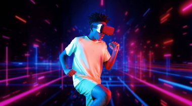 Parlak pembe ve mavi renkli soyut bir arka planda egzersiz yaparken VR kulaklık takan Afrikalı bir adam. Çekici erkek model beyaz gömlek giyerken spor yapıyor. Teknoloji. Yaratıcılık.