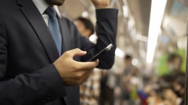 İş adamının elleri trende insanlarla çevriliyken telefona bakarken yakın çekim. Kafkas proje yöneticisi e-postaları kontrol ediyor, arka planı bulanık pazarlama stratejisi planlıyor. Sevinçli..