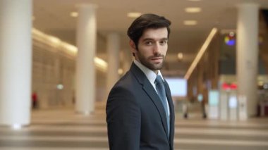 Profesyonel bir iş adamı kolları bağlıyken arkasını döner. Kafkasyalı mutlu yatırımcı, arka planı bulanık bir şekilde koridorda kollarını kavuştururken kameraya özgüvenle bakıyor. Portre. Sevinçli..