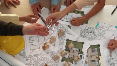 Mimari belge, ölçüm aracı ve ahşap blokların modern ofiste etrafa saçıldığı bir masa üzerinde yapı inşaatı ile ilgili mimar ve güvenlik mühendisi tartışması. Tanımlama.