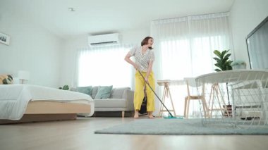 Modern apartman dairesinde dans ederken yerleri paspaslayan beyaz bir hizmetçi. Mutlu enerjik anne ya da temizlikçi müzik eşliğinde oturma odasını temizlemekten zevk alır. Yaşam tarzı. Pedagoji.