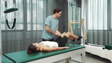 Pilates hocası, Cadillac teçhizatı üzerindeki bacak kaldırma egzersizi sırasında bir müşteriye yardım ediyor. Öğrenci uzanıyor ve temel dayanıklılık ve bacak esnekliğini arttırmak için Cadillac 'ın üzerinde bacak daire çiziyor. Alışkanlık.