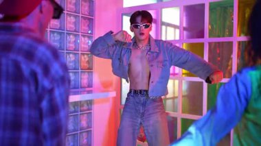 Ortasında dans eden profesyonel mutlu hipster onu alkışlayan çeşitli arkadaşlarıyla dans ediyor. Çekici Asyalı kırığı gece kulübünde neon ışığıyla enerjik adımlar atıyor. Mutluluk.