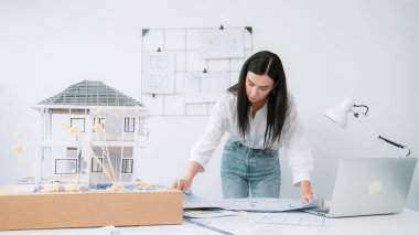 Genç, güzel beyaz bir mimar masanın üzerine plan koyar ve ev modeliyle karşılaştırırken, modern ofisteki fahişe modellerini dikkatlice incelerken arkadaki çizgilerle karşılaştırır. Tertemiz..