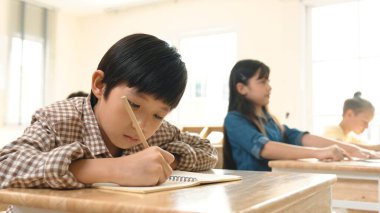 Yetenekli Asyalı öğrenci yazılarını kapatın ya da sınav sırasında not alın. Sınıfta çok kültürlü ödevler yaparken ilkokul öğrencisi kâğıt üzerinde çalışıyor. Eğitim konsepti. Pedagoji.