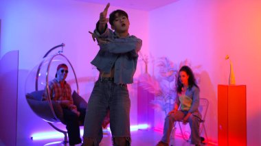 Çok kültürlü bir arkadaş kürsüde otururken Asyalı yetenekli bir dansçı modern müziğe geçiyor. Profesyonel dansçı, hipster takımı tezahürat yaparken ve desteklerken enerjik adımlar atıyor. Mutluluk.